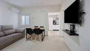 A modern living space with a sofa, dining table, chairs, a TV, and a kitchen in the background. - Holiday Home 'Camposoto' with Private Pool, Wi-Fi and Air Conditioning (San Fernando)