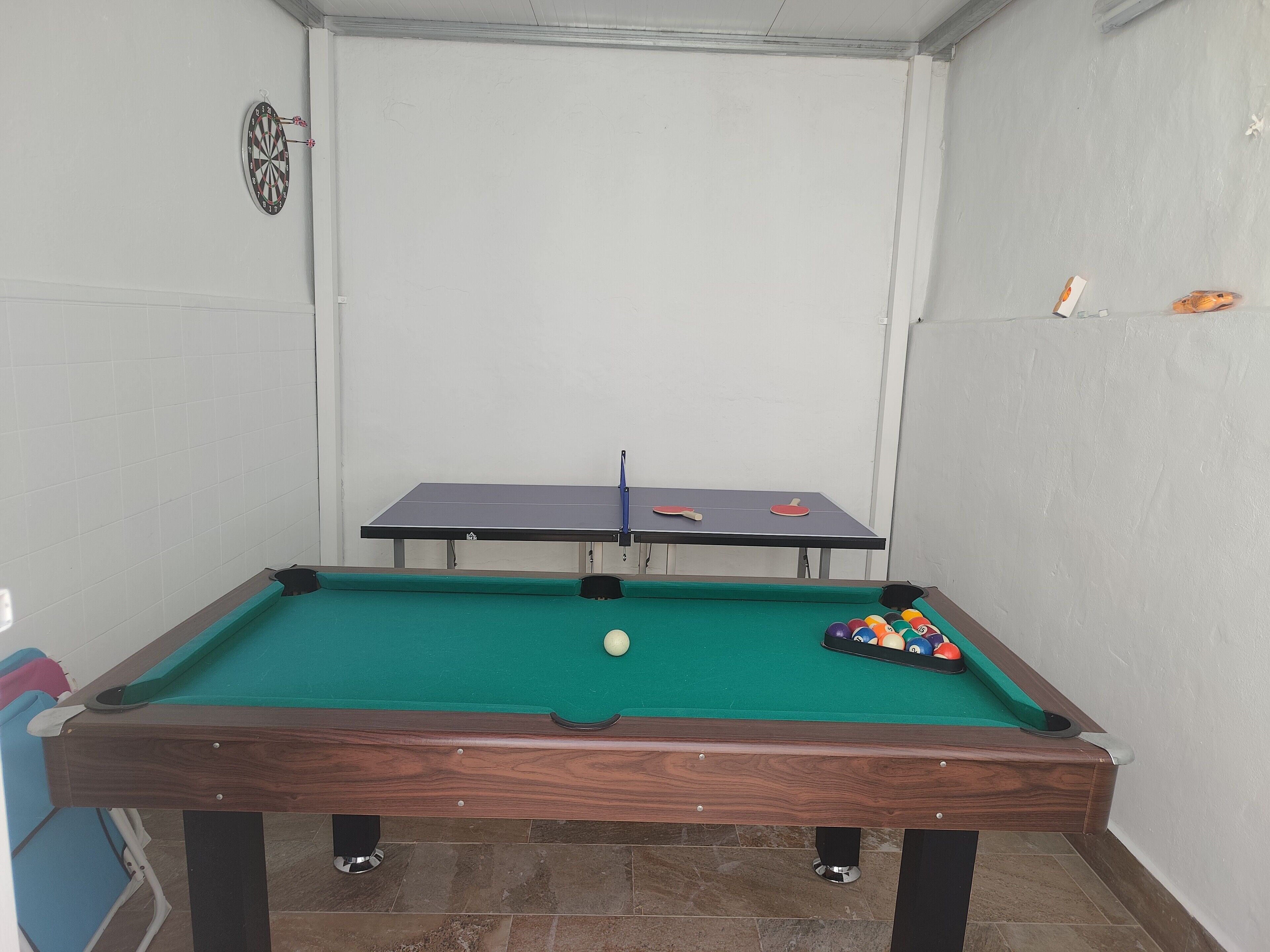 A pool table with a green felt surface, two red and white table tennis paddles, and a set of colorful pool balls.