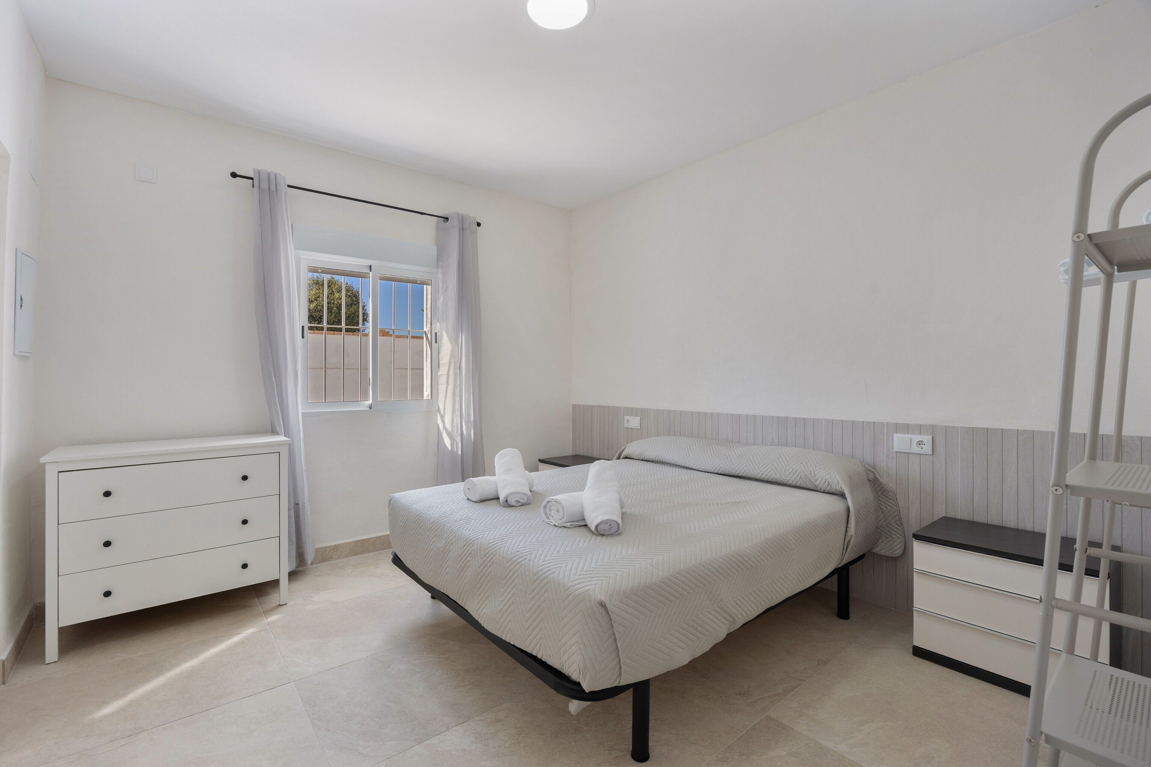 A bedroom with a bed, a nightstand, a dresser, and a window with curtains.