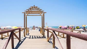 A wooden boardwalk leading to a beach with umbrellas and people.