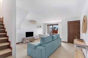 A modern living room with a sofa, a TV, a dining table, and a staircase.