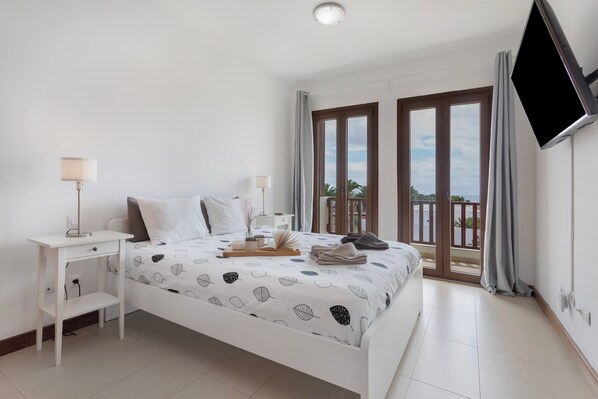A bedroom with a bed, bedside tables, a TV, and a balcony with a view.