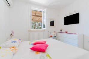 Un dormitorio con cama, ventana, cómoda y televisor en la pared.