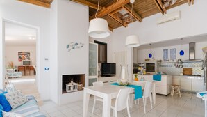 A modern kitchen with white cabinets, a dining area with a white table and chairs, and a living room with a striped sofa.