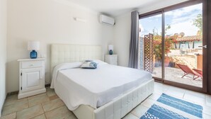 A bedroom with a bed, bedside tables, an air conditioning unit, and a view of the outside.