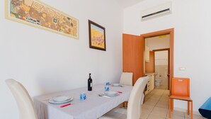 Un coin repas avec une table dressée pour quatre personnes, des chaises, un tableau accroché au mur et une porte ouverte donnant sur une salle de bain.
