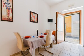 Un coin repas avec une table dressée pour quatre personnes, un téléviseur fixé au mur et une porte donnant sur l’extérieur.
