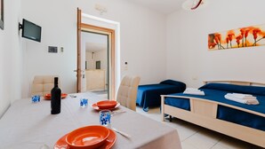 A hotel room with a dining table set, a bed with blue bedding, a painting on the wall, and a television mounted on the wall. - Holiday Home 'La Casetta 462' with Wi-Fi (Torre San Giovanni)