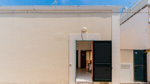 A building with a beige facade, a door with a black shutter, and a small window with a spherical object on top. - Holiday Home 'La Casetta 462' with Wi-Fi (Torre San Giovanni)