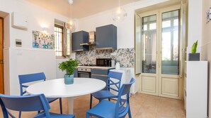 Eine moderne Küche mit Essbereich, inklusive rundem Tisch, blauen Stühlen, einem Blumentopf und einem großen Fenster.