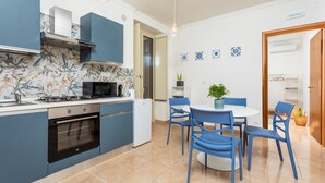 Eine moderne Küche mit blauen Schränken, einem Gasherd, einem Backofen und einer Mikrowelle. Ein Esstisch mit blauen Stühlen und einem Blumentopf sind ebenfalls vorhanden.