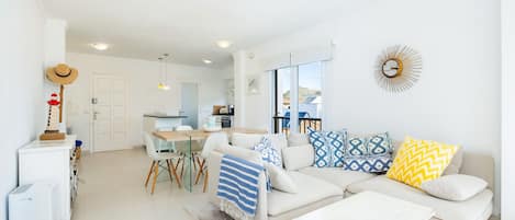 A modern living room with a sofa, coffee table, and a dining area with chairs and a table.