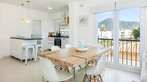 A modern kitchen with white cabinets, a dining table with chairs, and a view of the city through large windows. - Apartment Planeta Mallorca in Puerto de Pollensa with Sea Views, Wi-Fi, and Air Conditioning (Unknown)