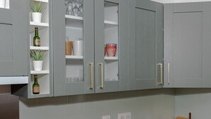 Una cocina con armarios grises, estantes blancos y encimera de madera.