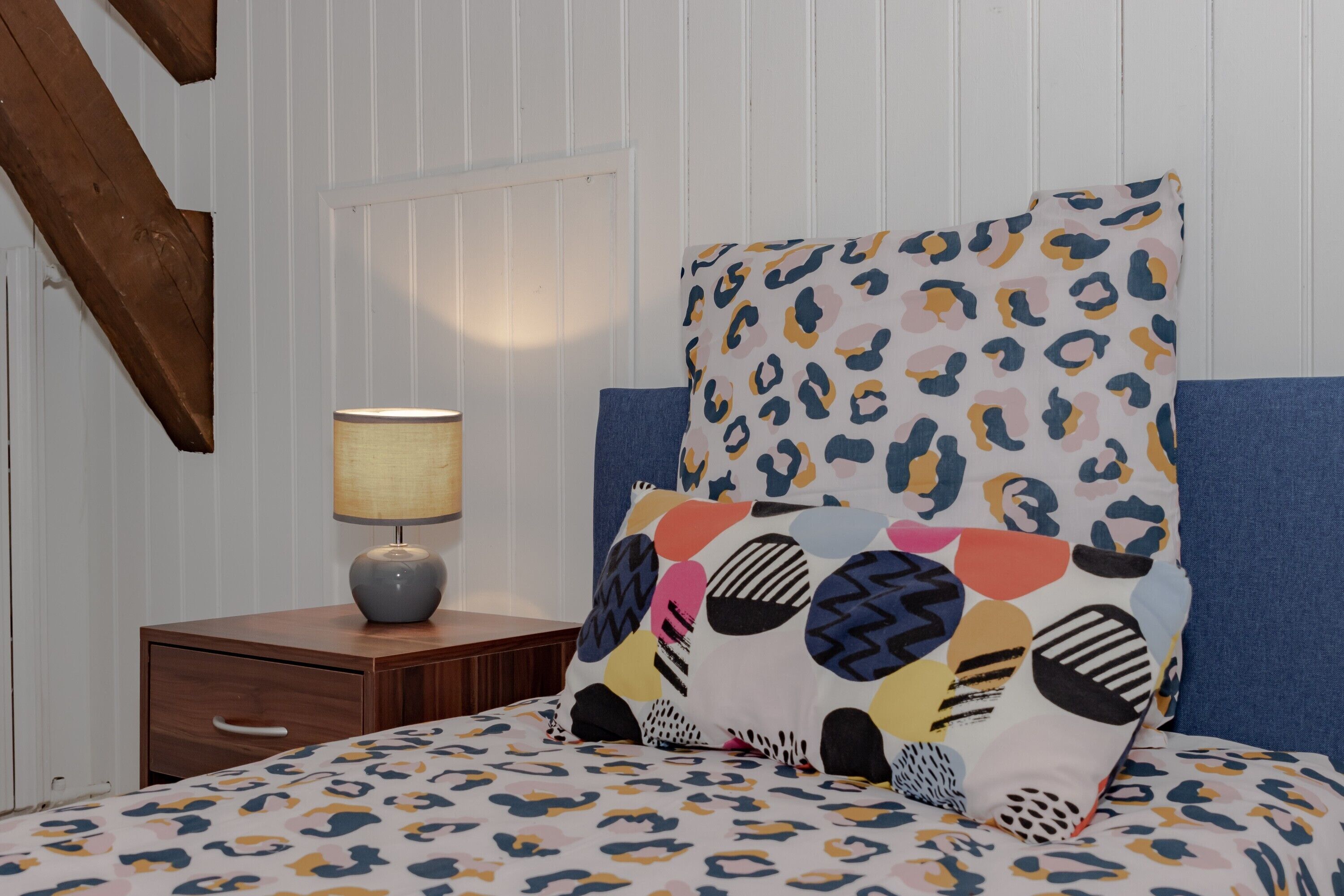 A bedroom with a bed, a nightstand with a lamp, and a window with blinds.