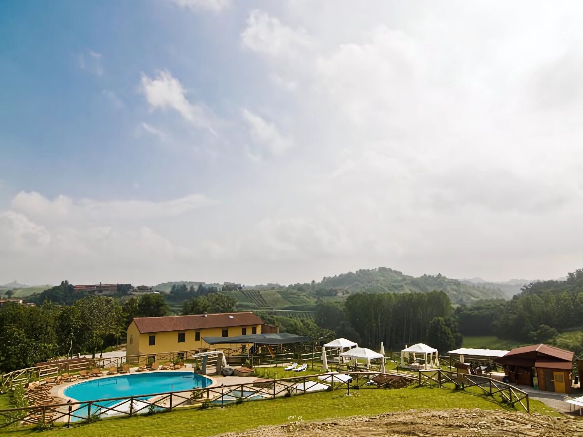 A pool area with lounge chairs, a building, and a hilly landscape in the background.