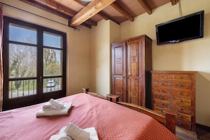 A bedroom with a bed, a wooden dresser, a television, and a window with a view of the outside.