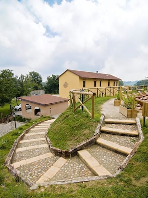 A building with a yellow facade, a stone pathway leading to it, and a small garden area with wooden benches.