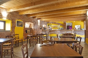 A restaurant with wooden tables and chairs, brick walls, and a yellow accent wall.