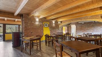 Ein Restaurant mit Holztischen und -stühlen, Backsteinwänden und einer hohen Decke.