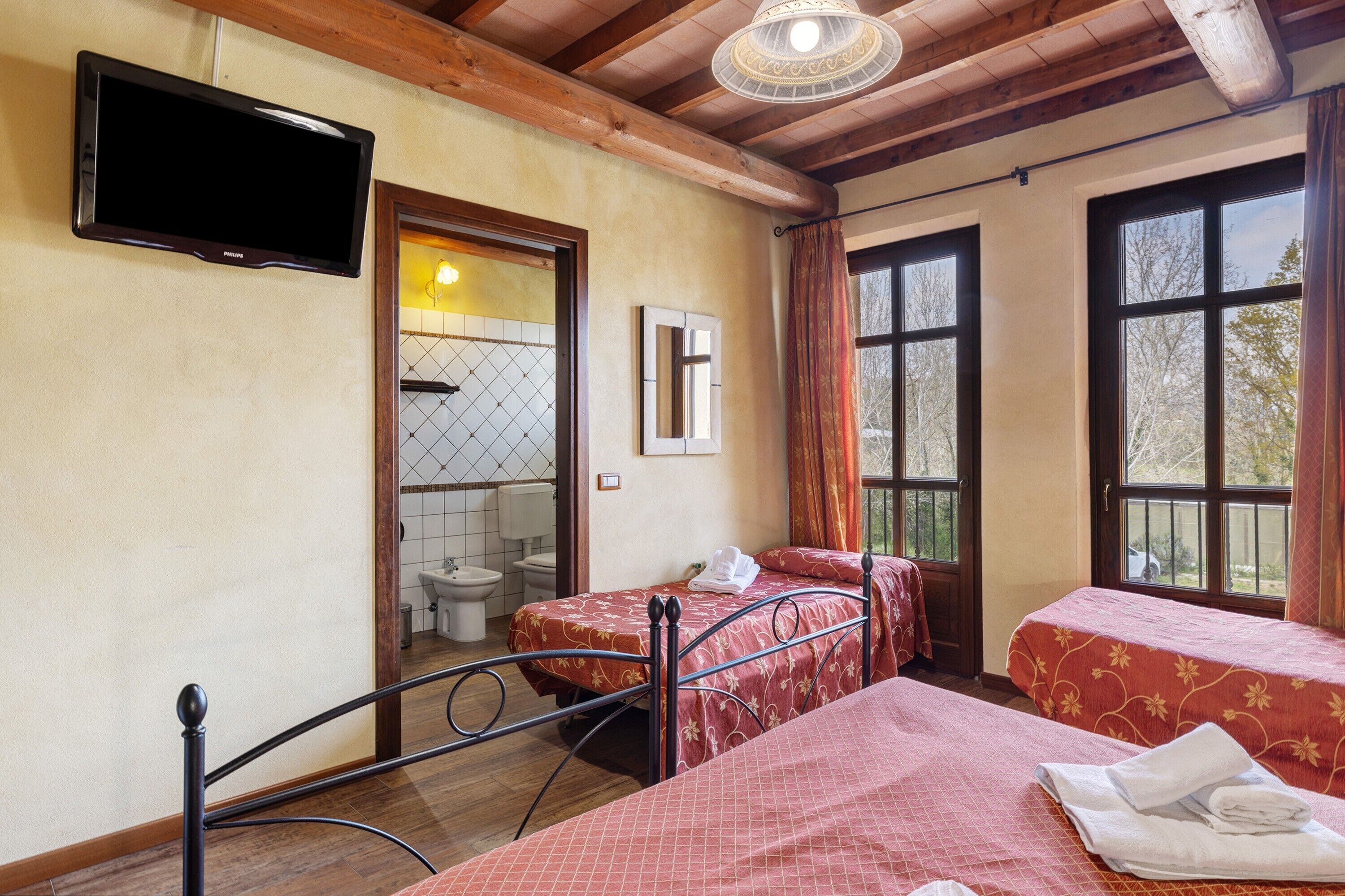 A room with two beds, a television, a bathroom, and large windows.