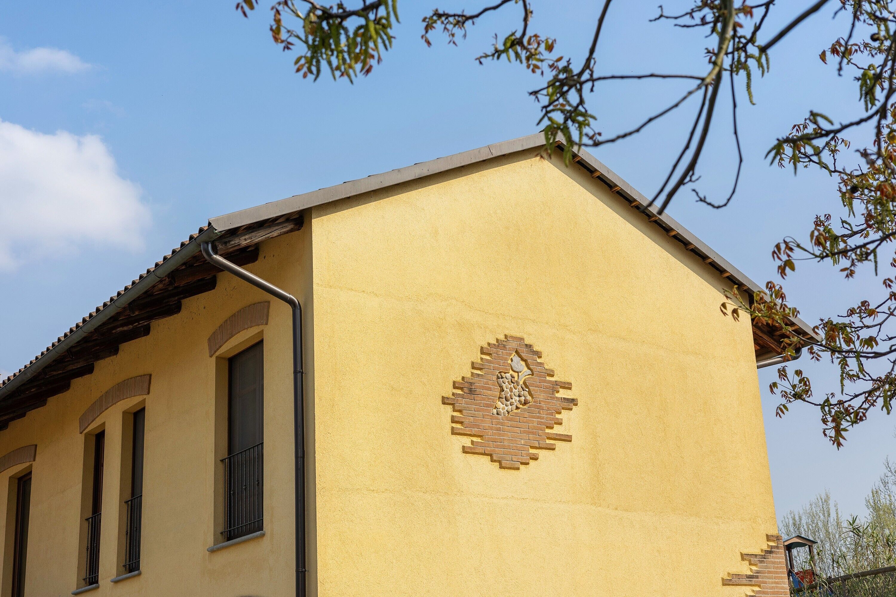 Un bâtiment à la façade jaune, avec un motif en briques sur le mur et une fenêtre ornée d’un garde-corps en métal.