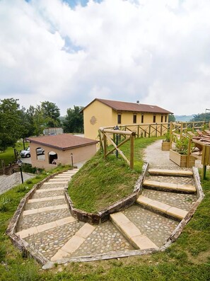 A building with a yellow facade, a stone pathway leading to it, and a small garden area with wooden benches.