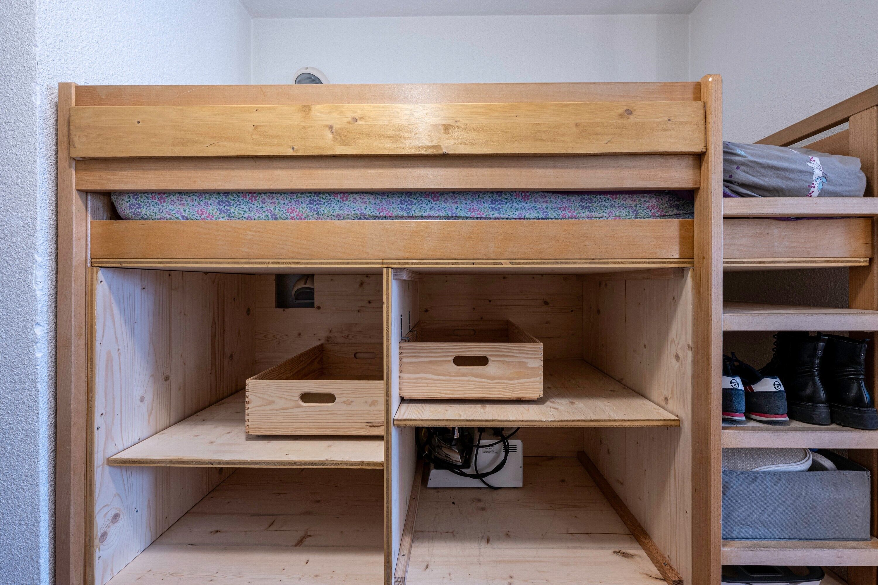 Una cama litera con estructura de madera, un colchón y un estante con zapatos.