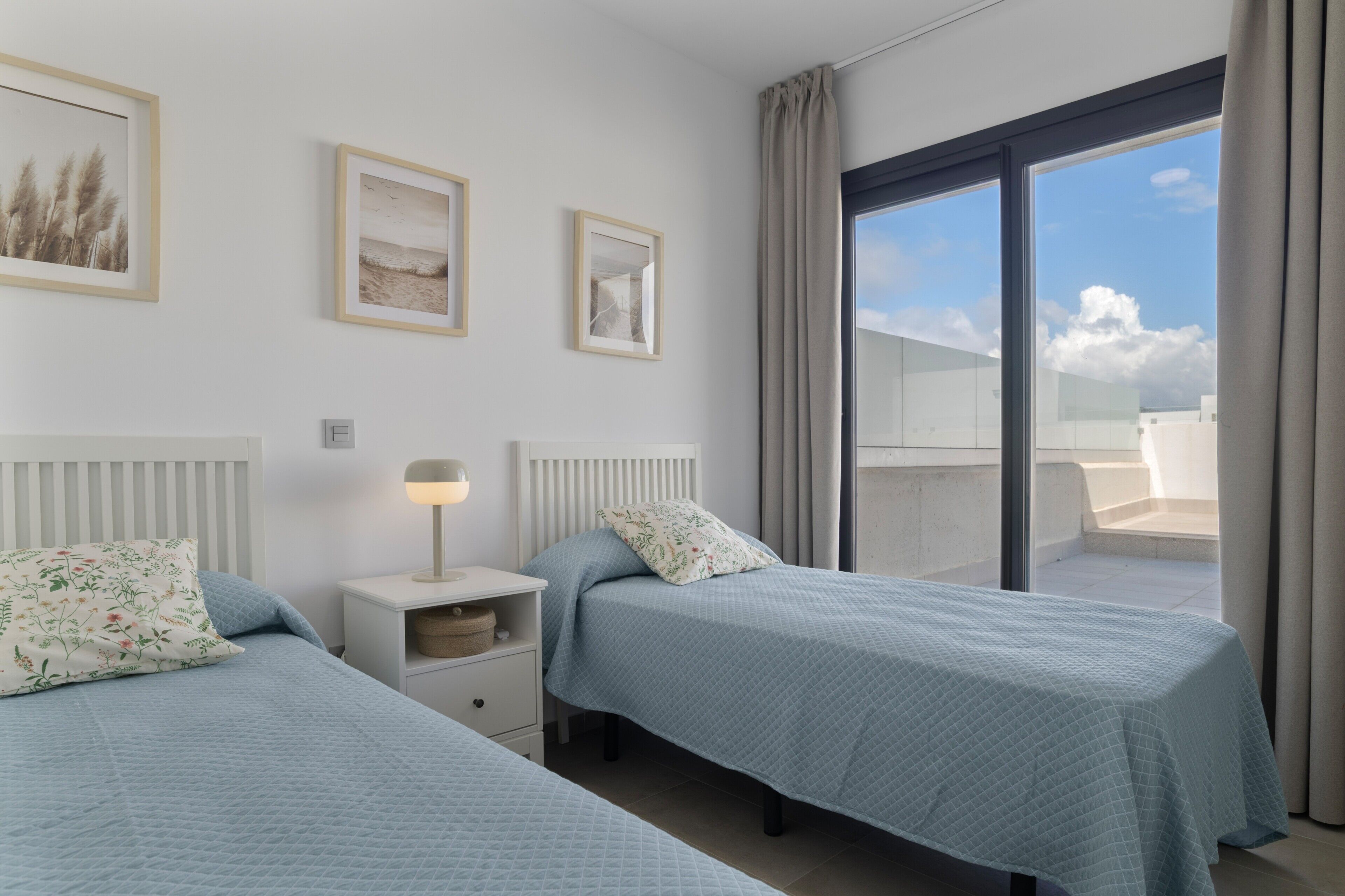 Un dormitorio con dos camas, una mesita de noche con lámpara y una ventana con cortinas.