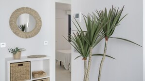 Um interior claro com um espelho redondo, cestos de vime e duas plantas altas com folhas verdes.