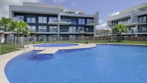 Um edifício moderno com piscina, cercado por palmeiras e um céu claro.
