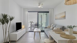 Uma sala de estar moderna com um sofá, uma mesa de jantar com jogos americanos, uma televisão em um móvel e um ventilador de teto.