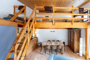 Una habitación estilo loft con una escalera de madera, una mesa de comedor con sillas y una zona de cocina.