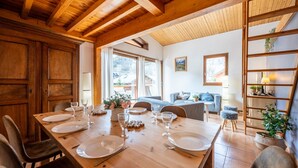 A dining area with a wooden table set for four, a sofa, and a bookshelf.