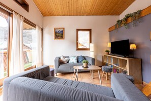 Un salón con un sofá gris, una mesa de centro, un televisor y una estantería.