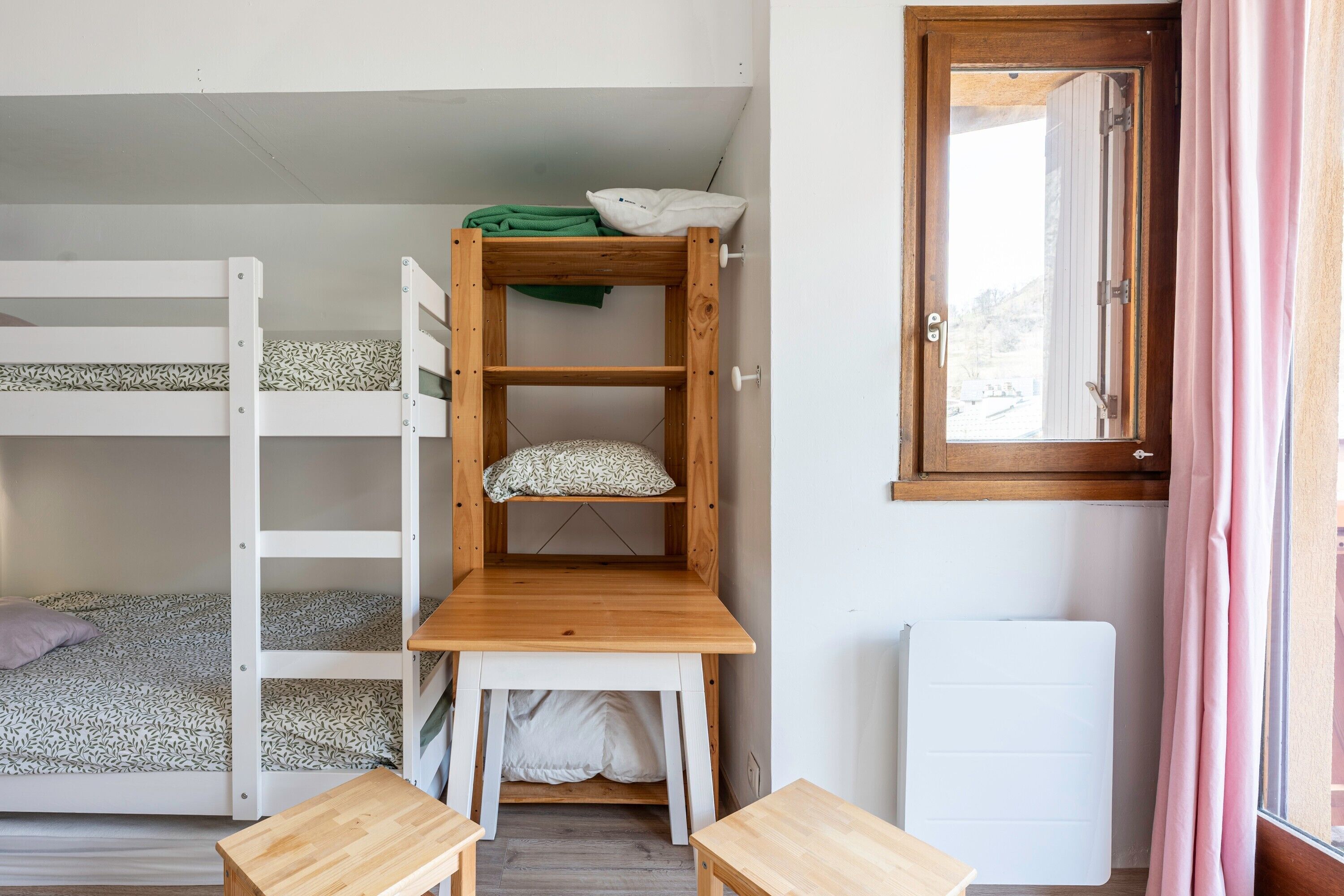 Een slaapkamer met een stapelbed, een houten bureau en een radiator.