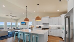 Una cocina moderna con armarios blancos, una isla grande con taburetes y vistas al océano.