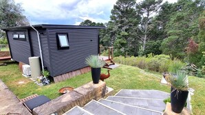 A compact, modern cabin with a sloped roof, a small deck, and a stone staircase leading to a wooden deck area. - Tranquil Studio Retreat in Leura with Private Bush Outlook. (Leura)