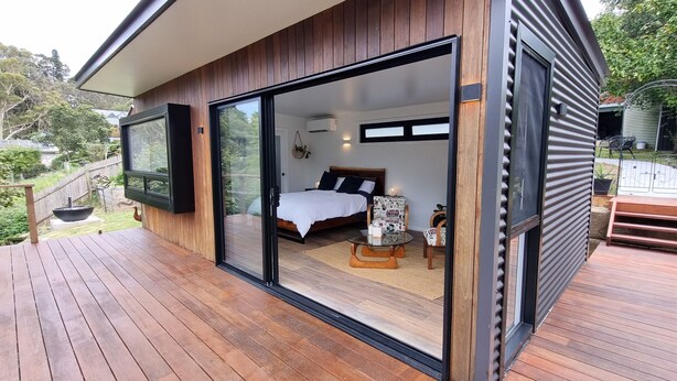 A modern house with a deck, a bedroom with a bed and a small table, and a large window. - Tranquil Studio Retreat in Leura with Private Bush Outlook. (Leura)
