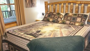 Un dormitorio con cabecera de madera, una cama grande con colcha estampada, vista a un balcón y un cuadro en la pared.