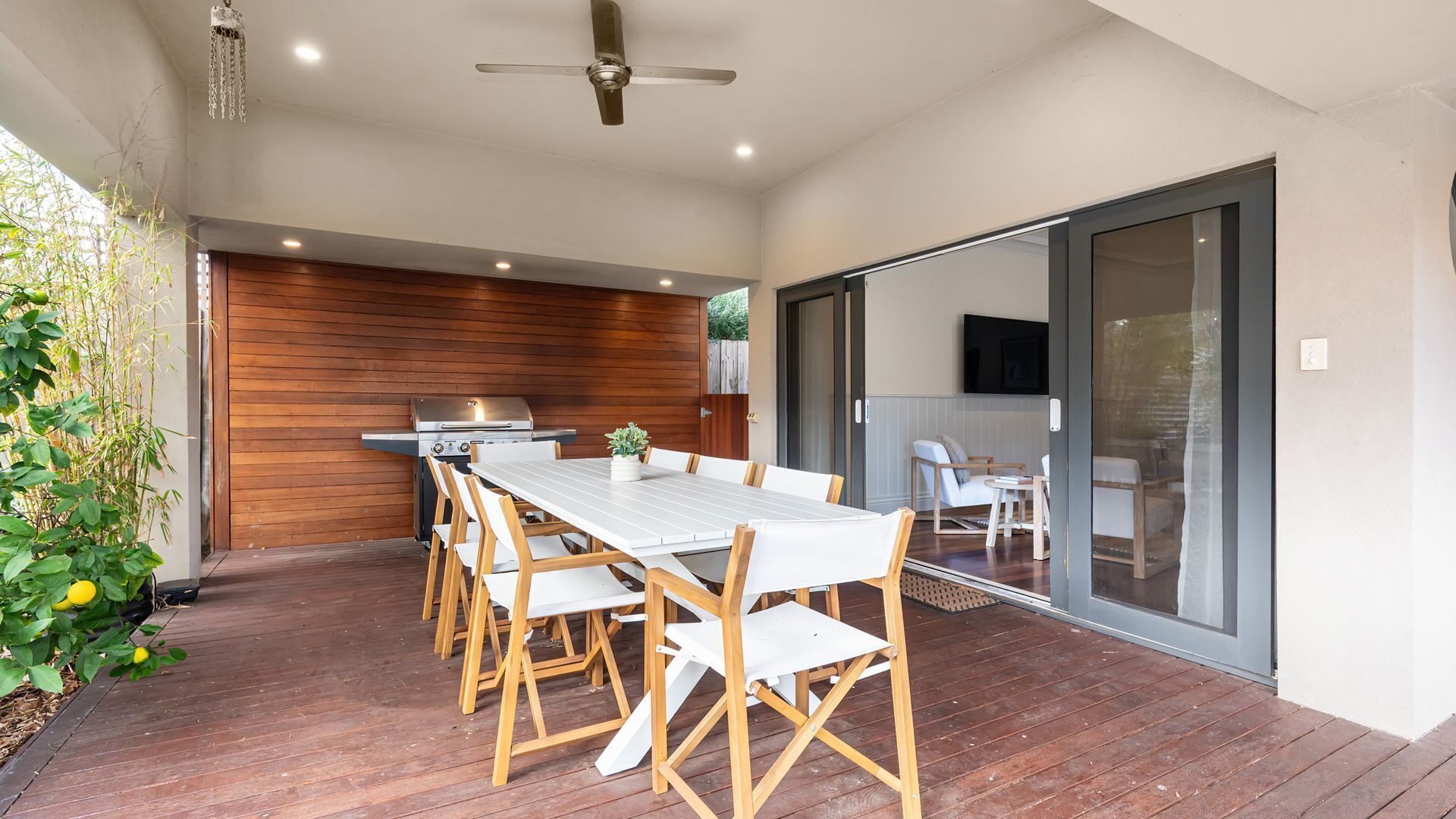A modern outdoor dining area with a wooden deck, a long white table, and chairs.