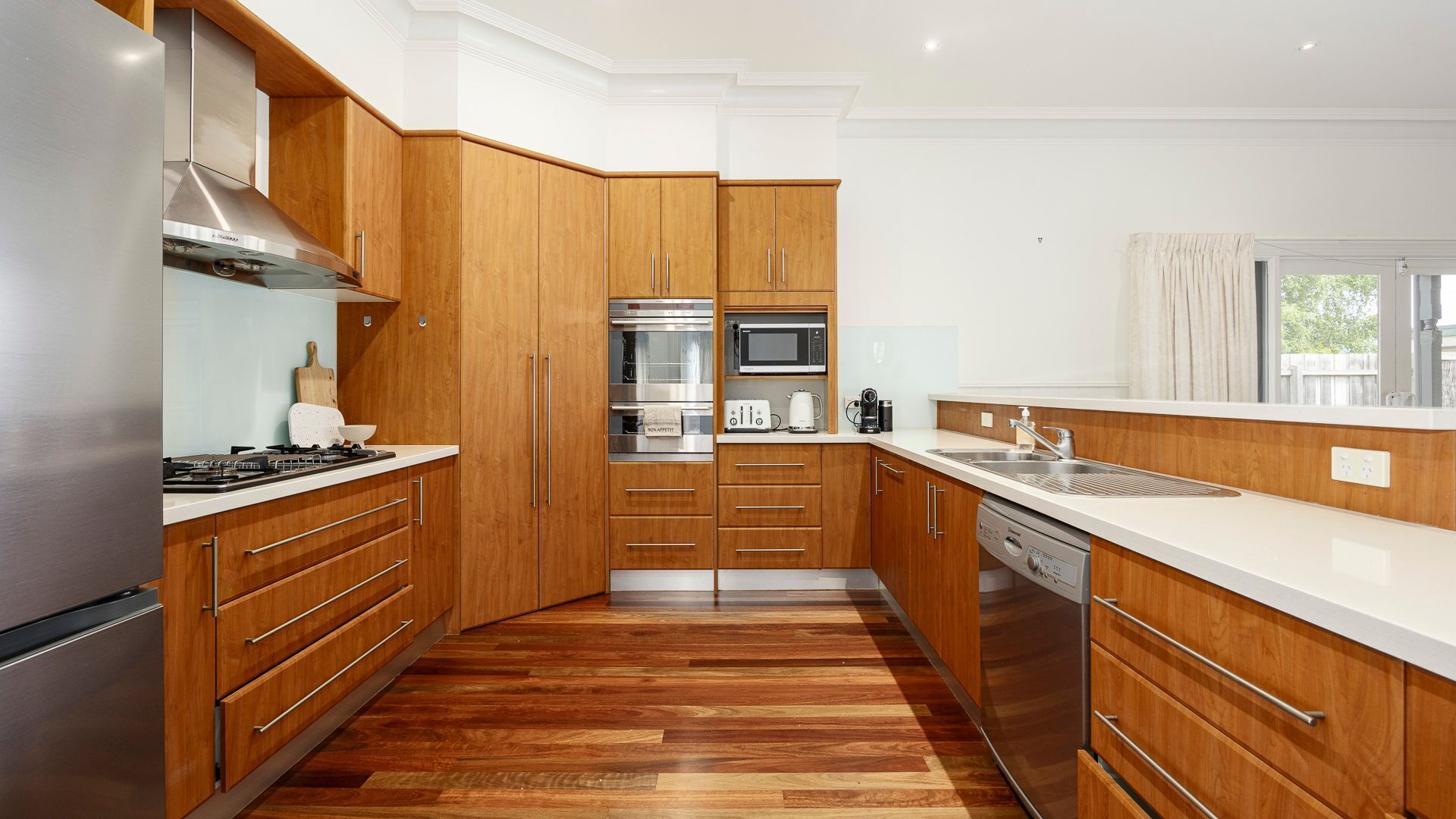 Una cocina moderna con armarios de madera, electrodomésticos de acero inoxidable y encimera blanca.