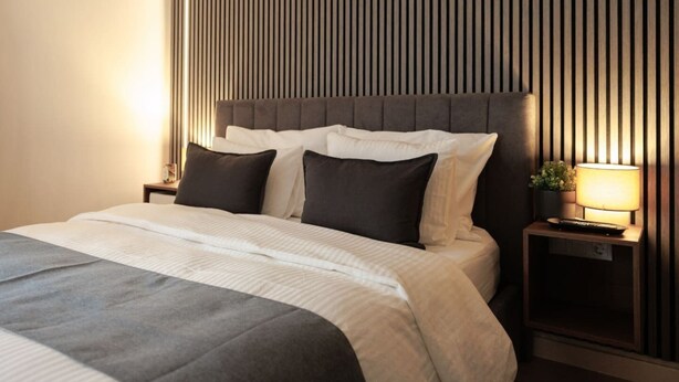 A neatly made bed with a grey and white duvet, a dark headboard, and a bedside table with a lamp and a small plant.