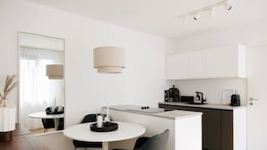 A modern kitchen with white cabinets, a dining area with a round table and chairs, and a pendant light.