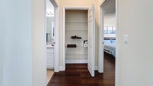 Un couloir étroit mène à un placard doté d’étagères, et la pièce adjacente contient un lit.