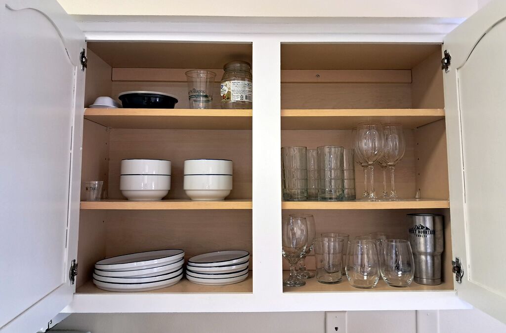 Un mueble con estantes que contiene diversos utensilios de cocina, incluyendo cuencos, platos y vasos.