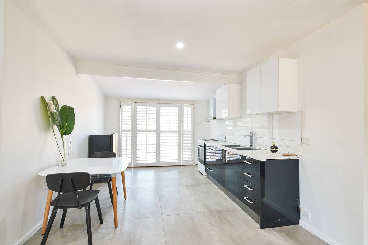 A modern kitchen with white cabinets, a black countertop, and a dining area with a white table and chairs.