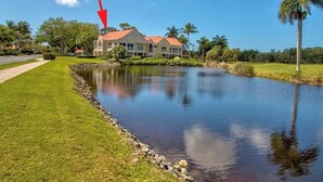 A house with a red roof, surrounded by a pond, palm trees, and a clear blue sky. - Naples Florida - This condo is like no other!! Windstar on Naples's Bay (Naples)