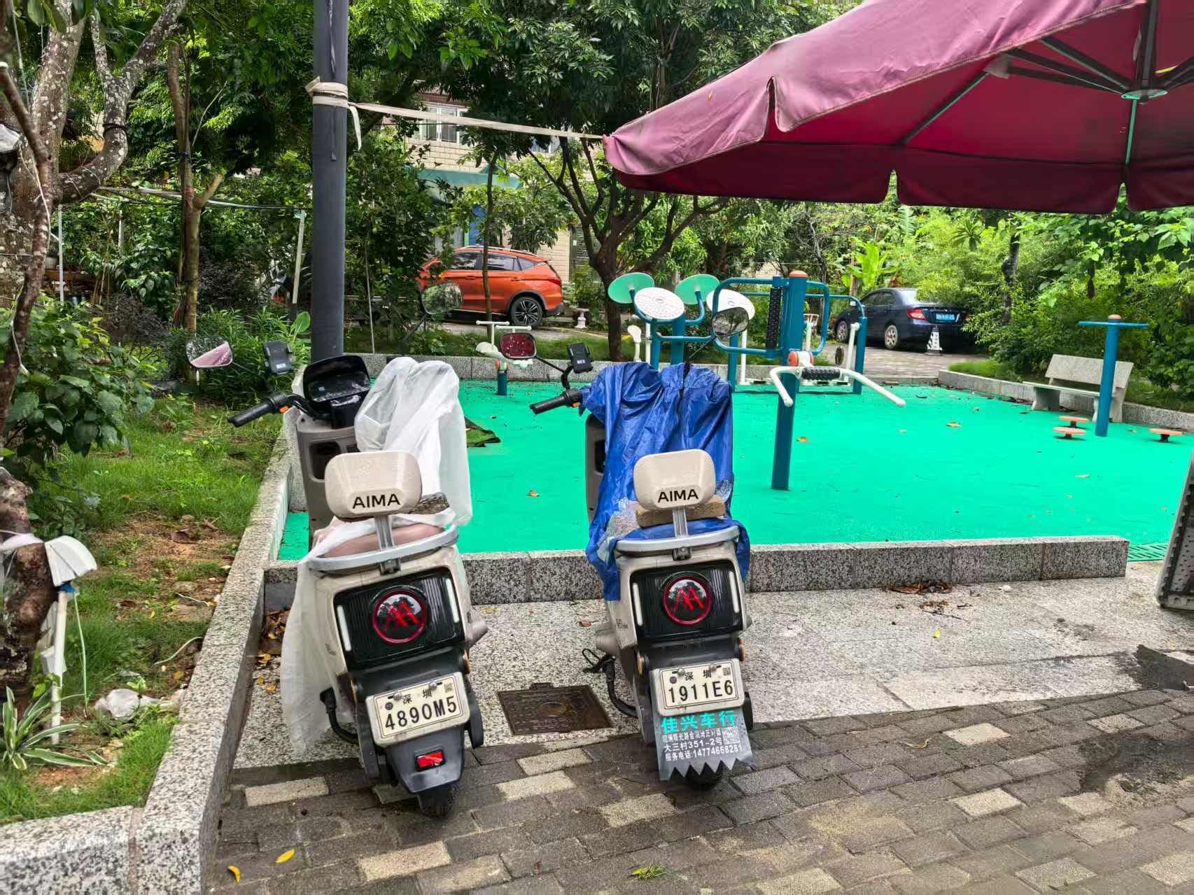 Two scooters parked near a green exercise area with a red umbrella overhead.