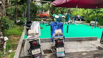 Two scooters parked near a green exercise area with a red umbrella overhead.